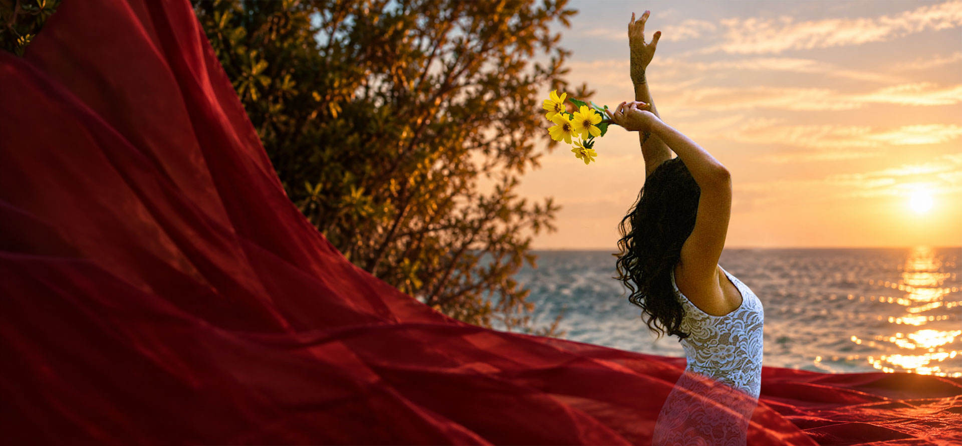 Adelina at the ocean holding yellow flowers toward the sunset