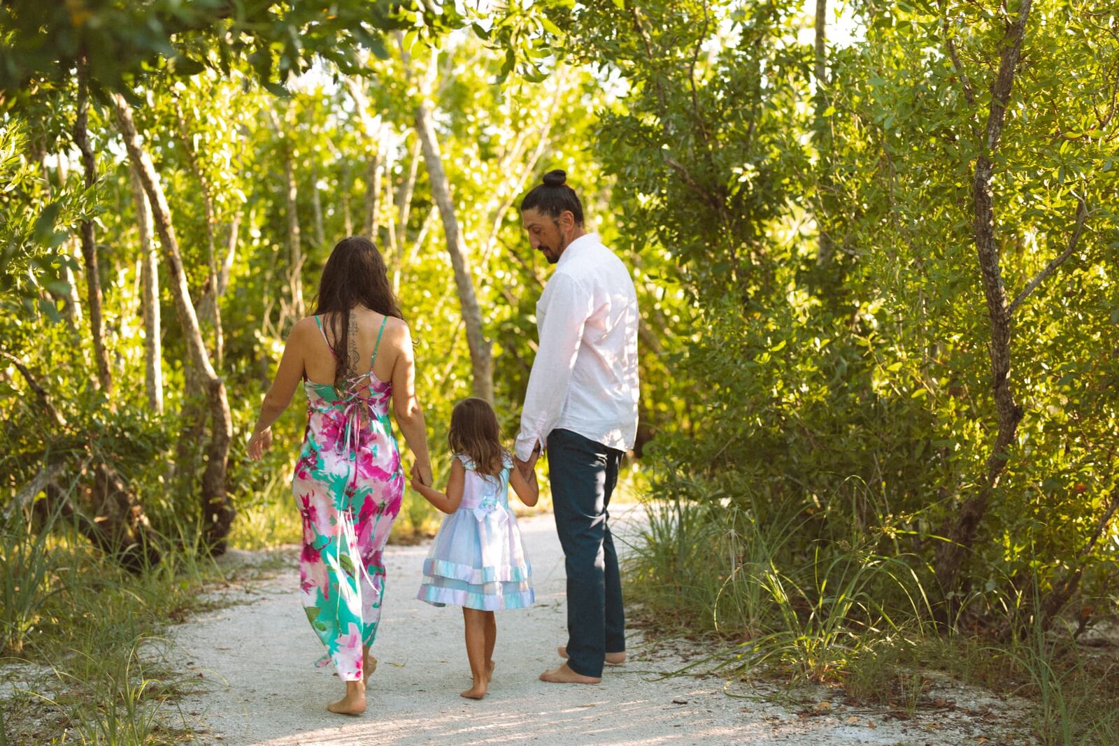 Adelina, her husband and their daughter walking hand in hand down a sunlit path