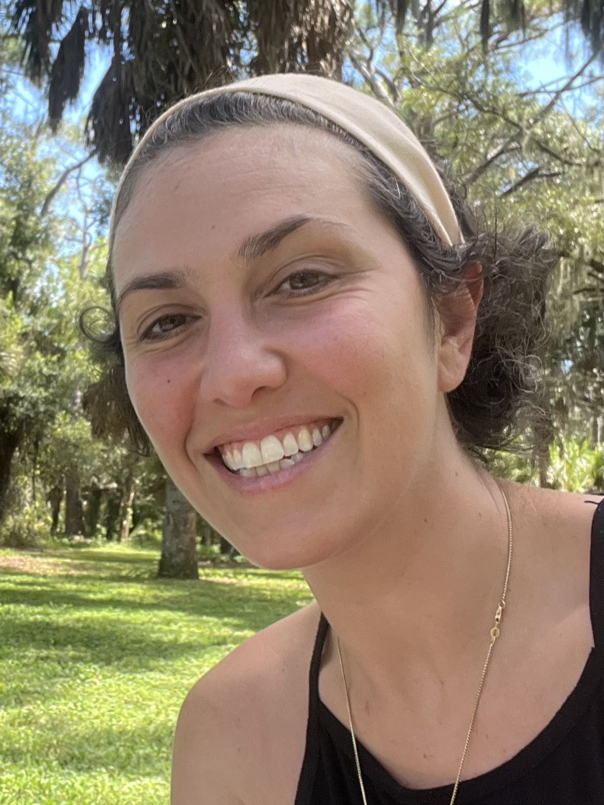 Adelina smiling outdoors in a park, seated on the grass with a picnic blanket beside her